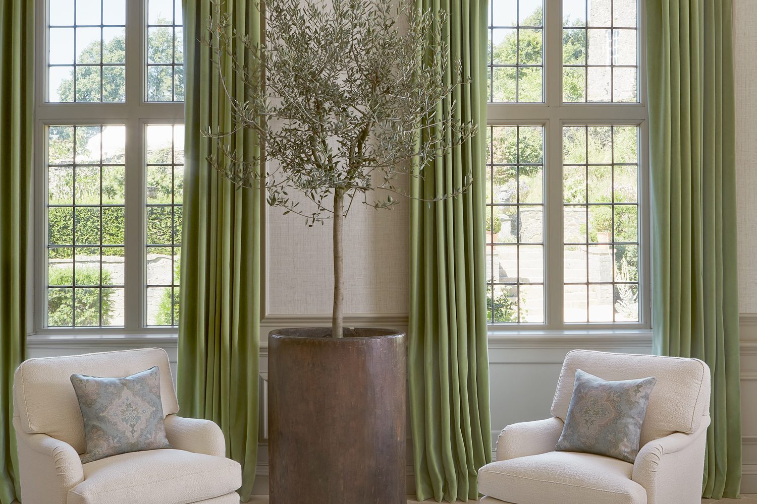 Colefax and Fowler : rideaux vert olive tendre et fauteuils blancs devant de grandes fenêtres