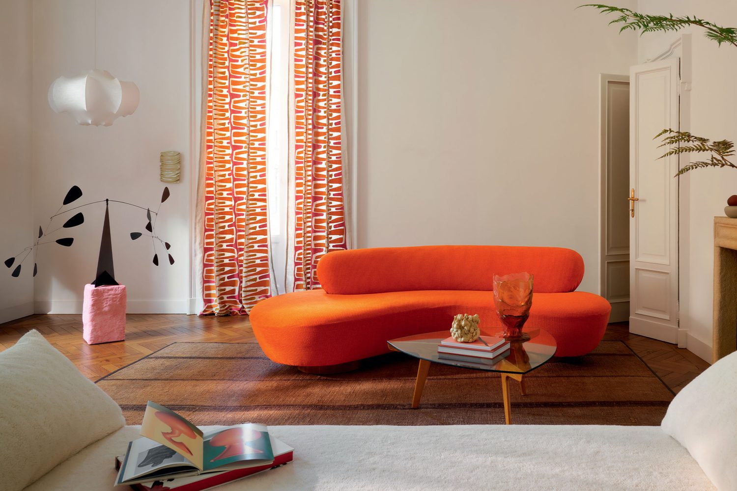 Élitis, Keep It Up : canapé orange et rideaux à motifs orangés dans un salon blanc
