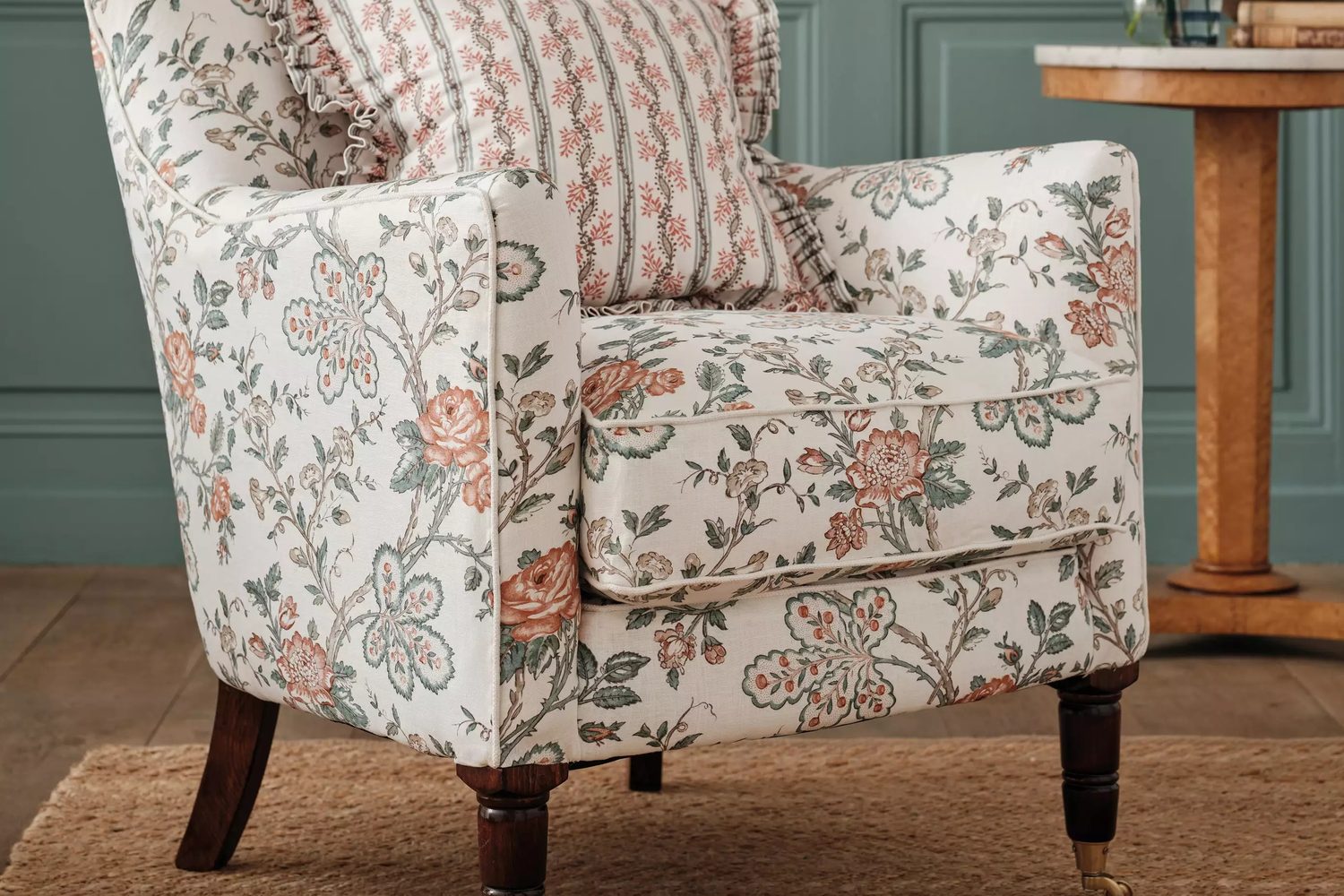 Osborne & Little, Dauphine : fauteuil au tissu floral crème et saumon devant un mur bleu canard